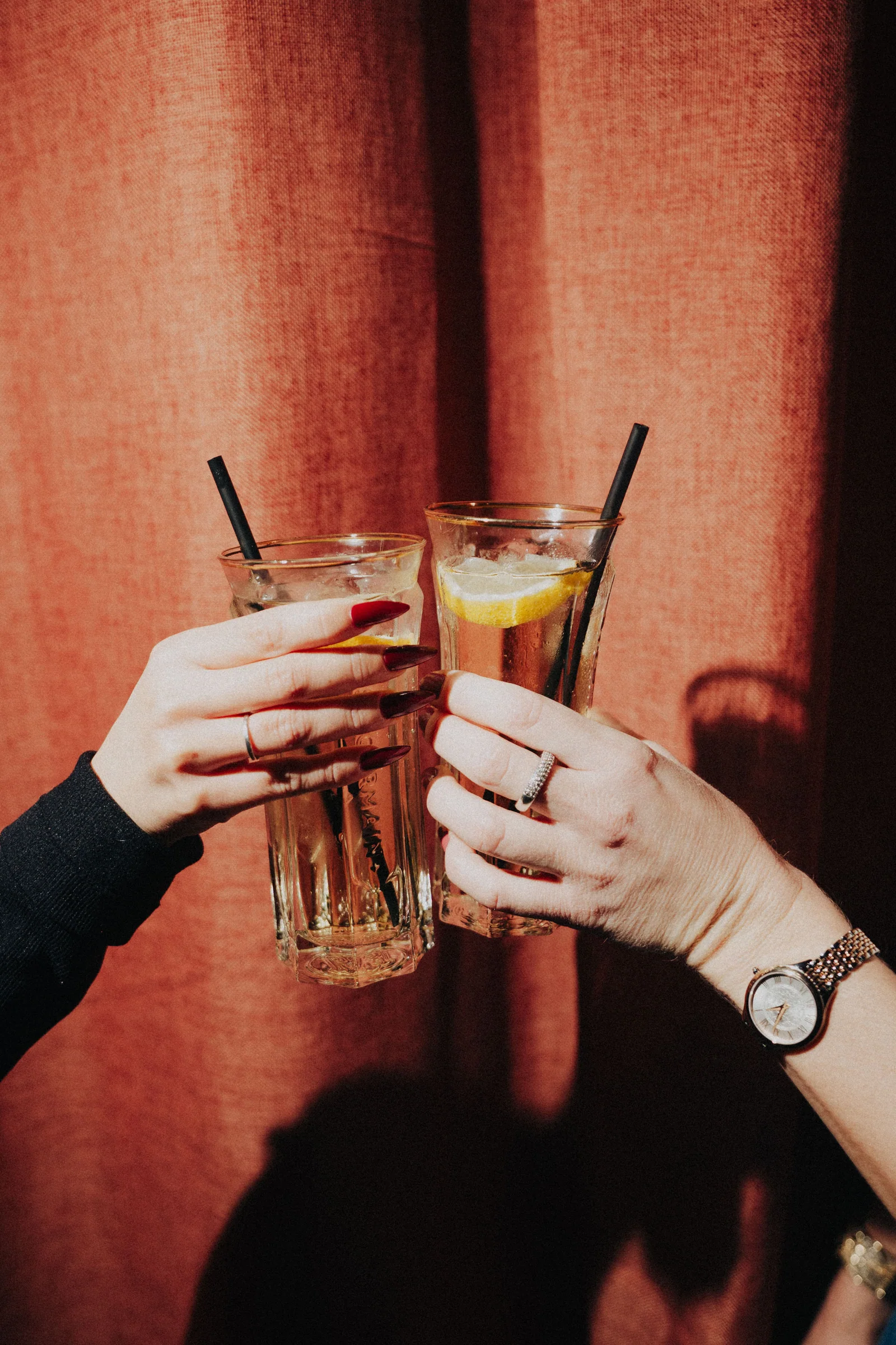 Deux mains rapprochent leurs verres devant un rideau rouge